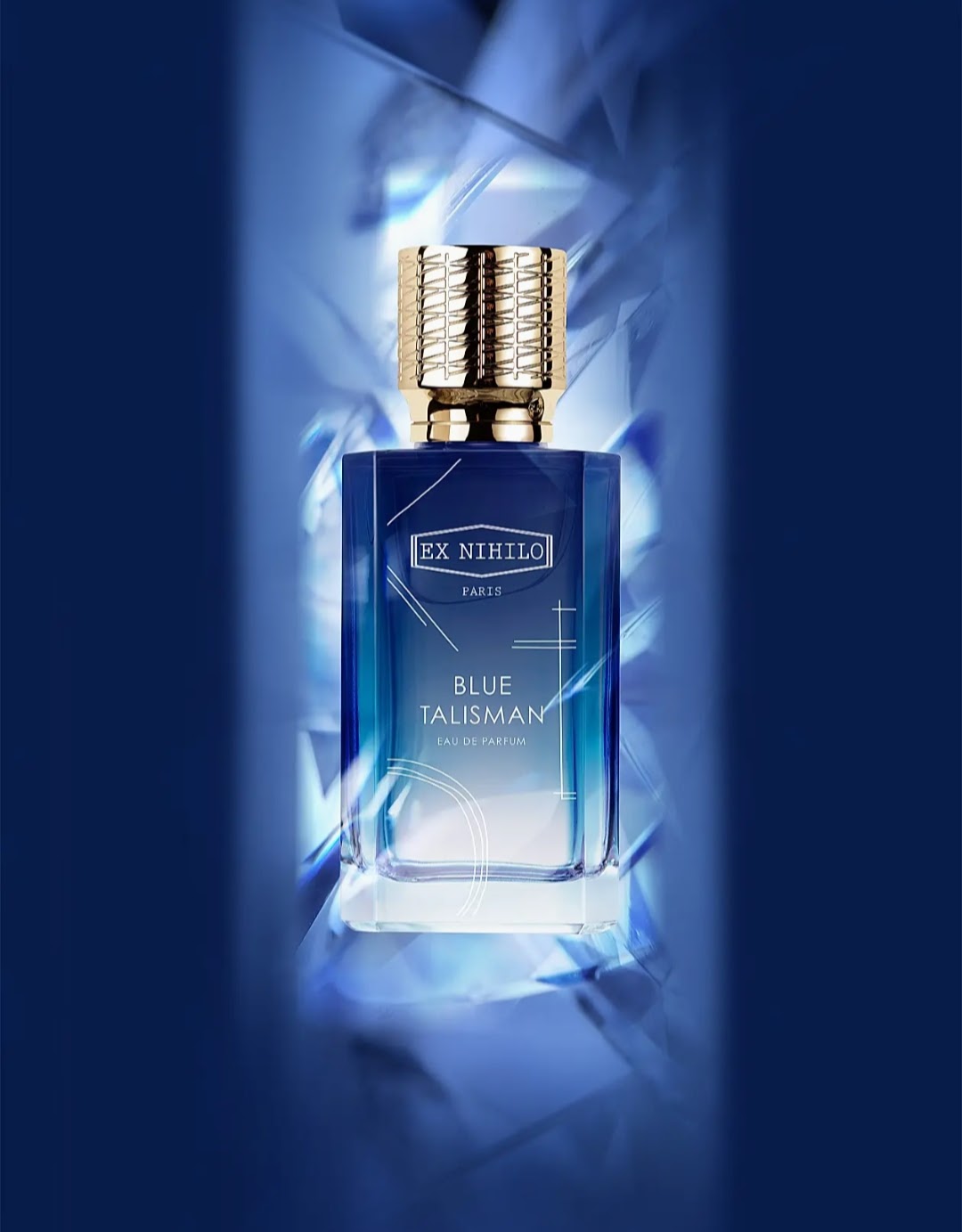 A bottle of EX NHILLO PARIS Blue Talisman Eau de Parfum, featuring a blue glass bottle and a textured gold cap, set against a dark blue background with dramatic light effects.