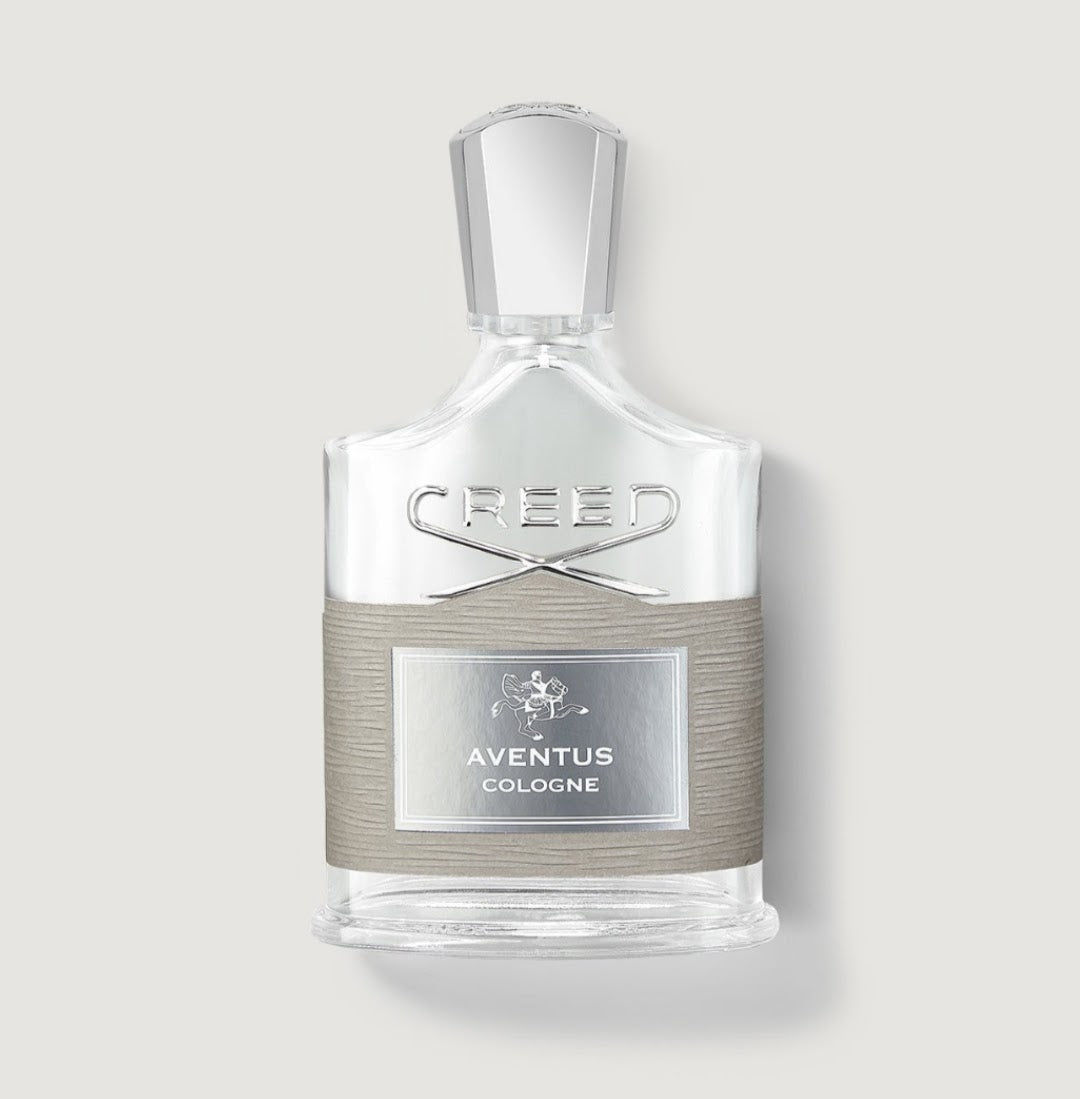 Creed Aventus Cologne perfume bottle with a clear glass body, silver cap, and a textured taupe band around the middle, on a light gray background.