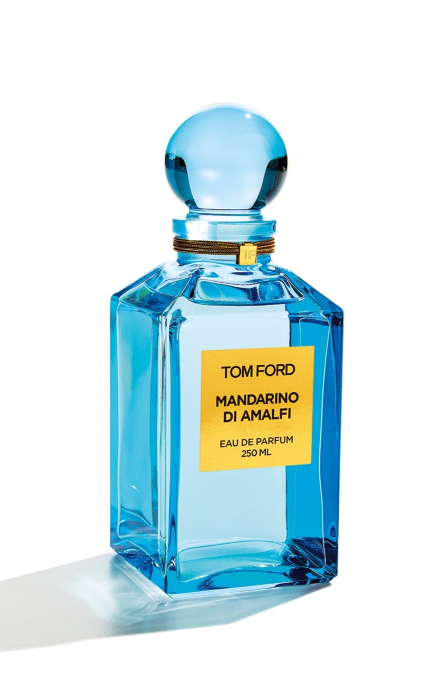 A Tom Ford Mandarin di Amalfi Eau de Parfum bottle, made of transparent light blue glass with a yellow label and a matching blue spherical cap, set against a plain white background.

